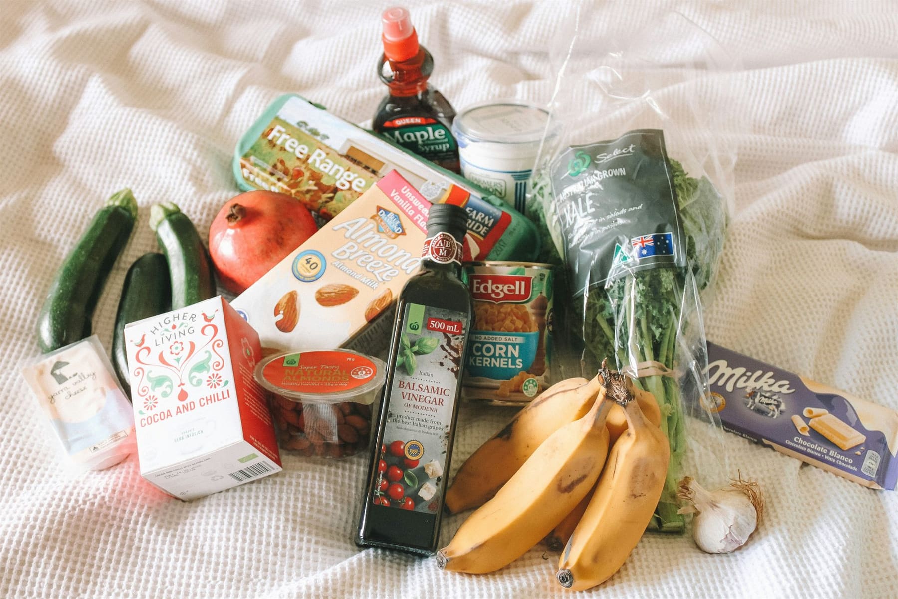 A fresh grocery haul — produce, pantry staples and treats — laid out on a white blanket